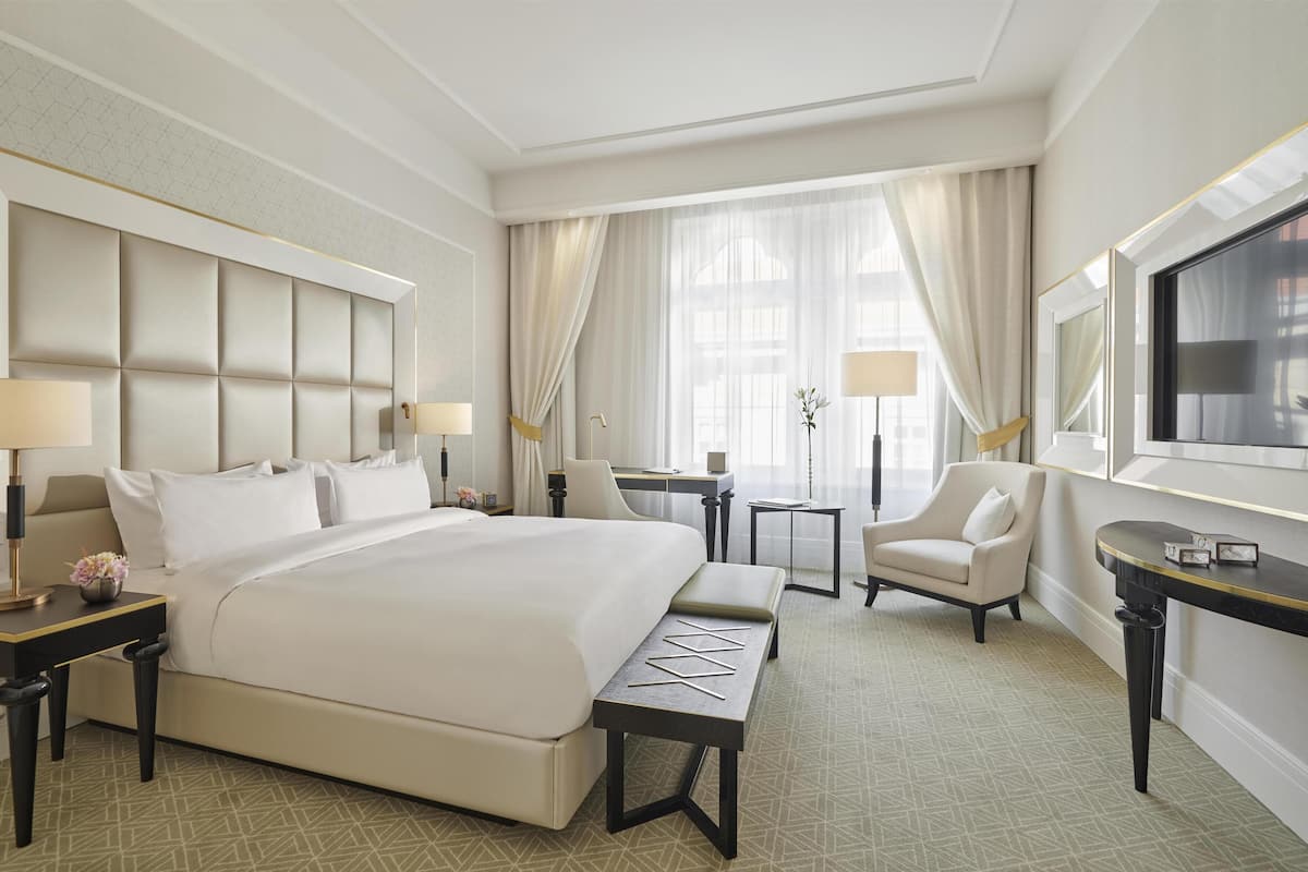 A hotel room with a large bed, a desk, a chair, a small table, and a TV.