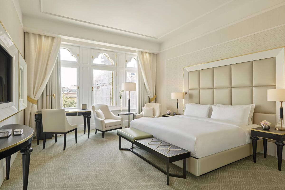 A hotel room with a large bed, two armchairs, a desk, and a small table.