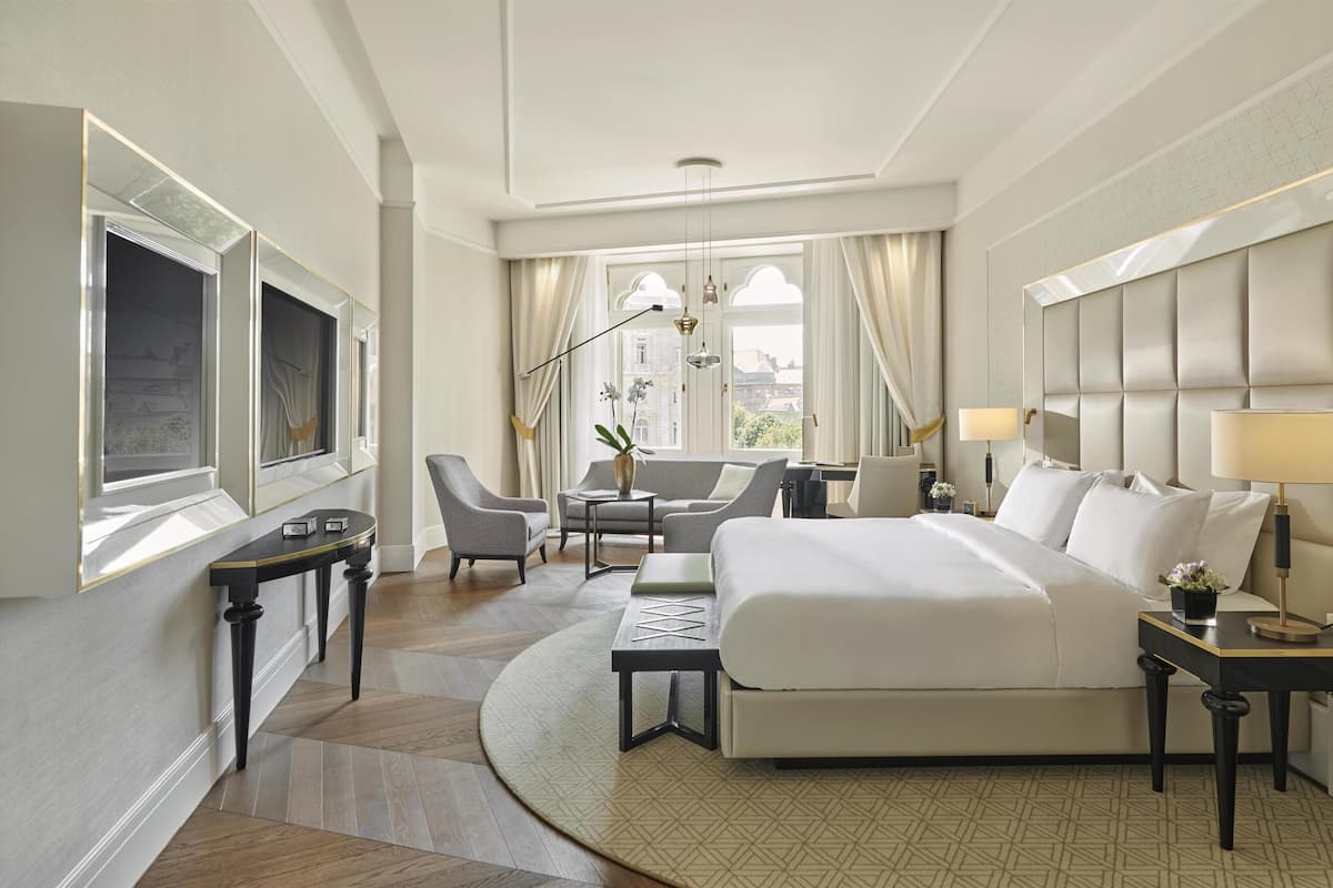 A hotel room with a large bed, a desk, a chair, a TV, and a window with curtains.