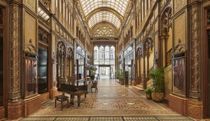 Un amplio pasillo con columnas ornamentales, un piano de cola y una alfombra estampada.