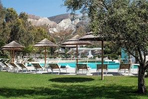 A pool area with sun loungers and umbrellas, surrounded by greenery and mountains in the background. - Mari del Sud Resort (Lipari)