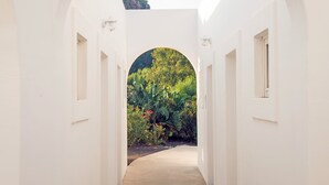 Ein weißer Korridor mit Rundbogenöffnungen, der in einen Garten mit üppiger Bepflanzung und Bergblick führt.