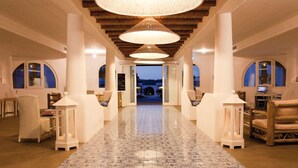 Eine Hotelhalle mit einem zentralen Gang, weißen Möbeln und großen Pendelleuchten.