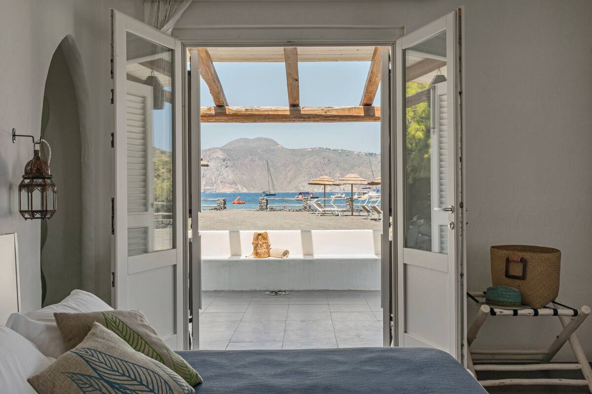An open bedroom with a view of a beach and boats.