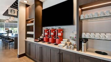 A modern kitchen with a coffee station, including multiple coffee dispensers and a large flat-screen TV.