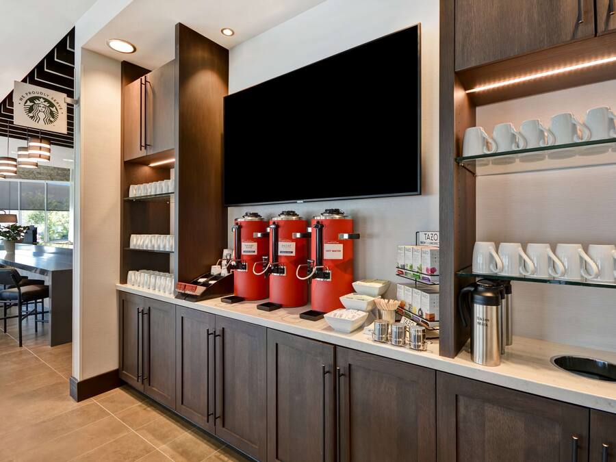 A modern kitchen with a coffee station, including multiple coffee dispensers and a large flat-screen TV.