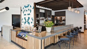 A modern bar area with a wooden counter, bar stools, and a potted plant. - Hyatt Place Fresno (Fresno)