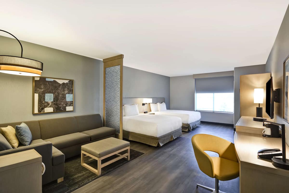 Ein Hotelzimmer mit einer Couch, zwei Betten, einem Schreibtisch und einem Sessel.