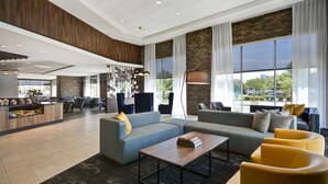 A spacious lobby with a modern design, featuring a seating area with sofas and armchairs, a coffee table, and a bar area with a counter and seating. - Hyatt Place Fresno (Fresno)