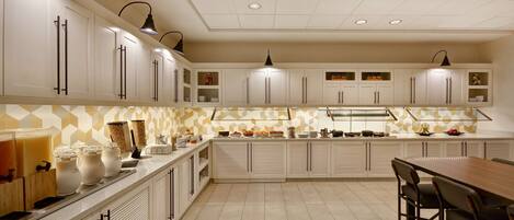 A modern kitchen with white cabinets, a wooden dining table, and pendant lighting.