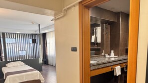 Una habitación de hotel con una cama, un baño con un espejo grande y suelo de madera.