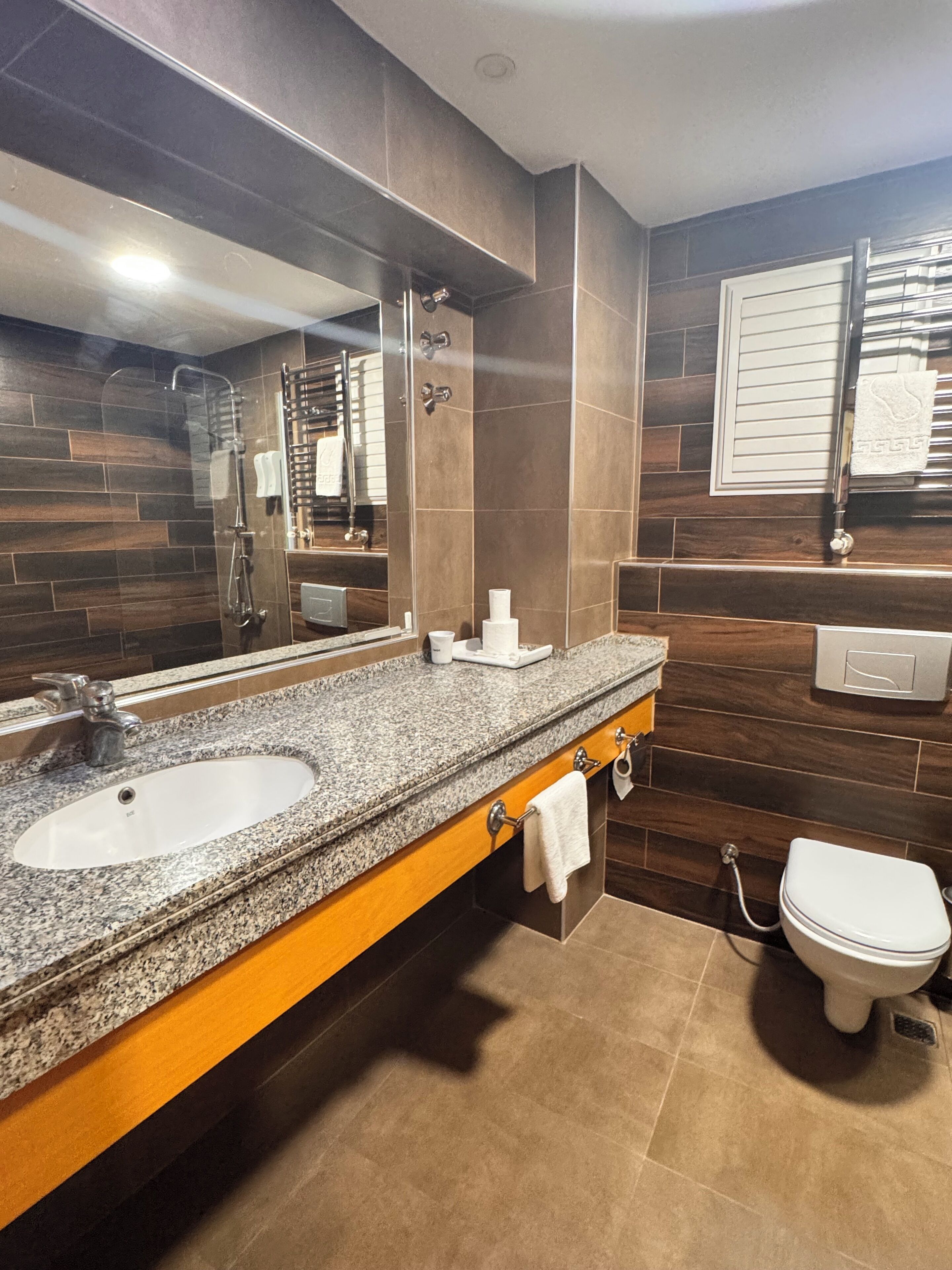 Une salle de bain moderne avec un lavabo à vasque en granit, un grand miroir, un porte-serviettes et des toilettes.