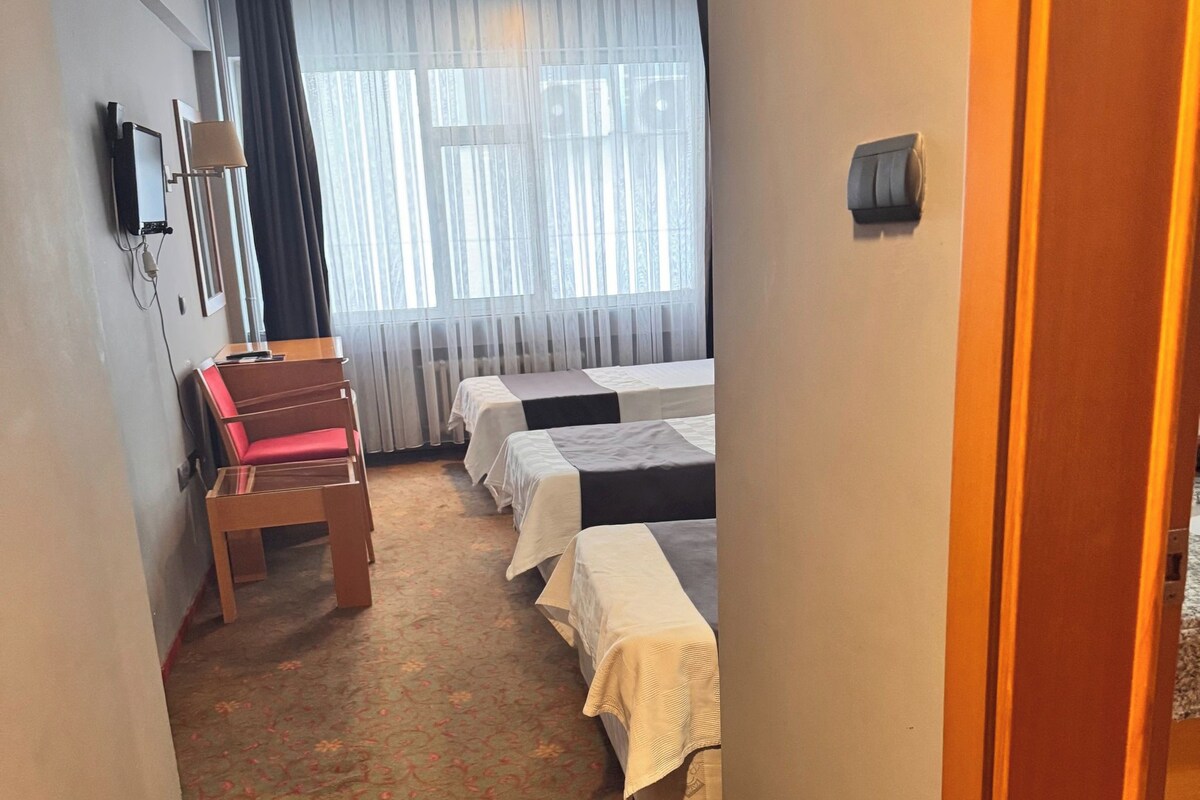 Habitación de hotel con un pasillo estrecho que conduce a una zona con dos camas y un escritorio con una silla.