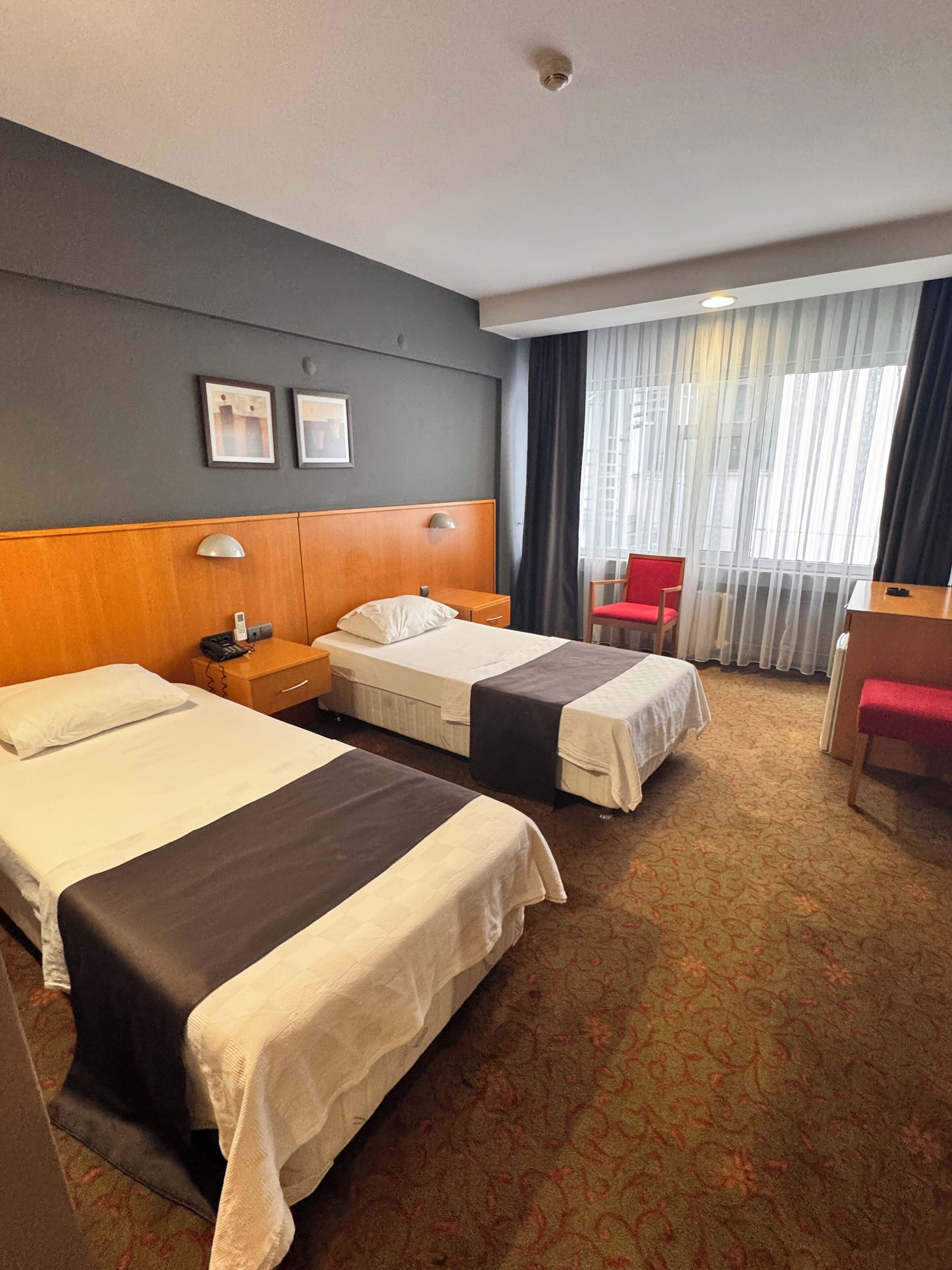 A hotel room with two beds, a desk, a chair, and a window with curtains.