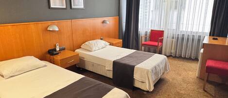 A hotel room with two beds, a desk, a chair, and a window with curtains.