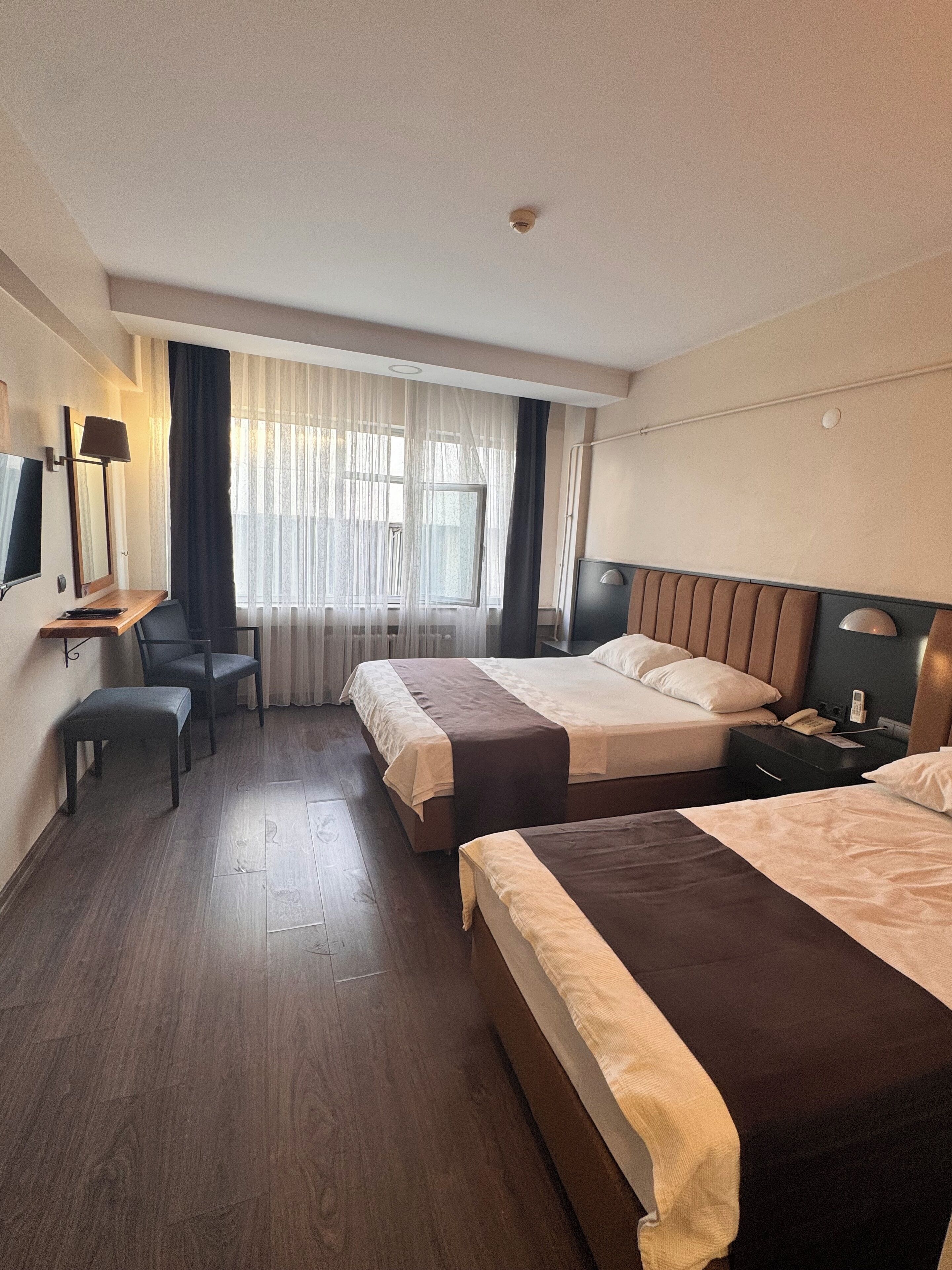 Habitación de hotel con dos camas, un escritorio, una silla, un televisor y una mesita de noche.