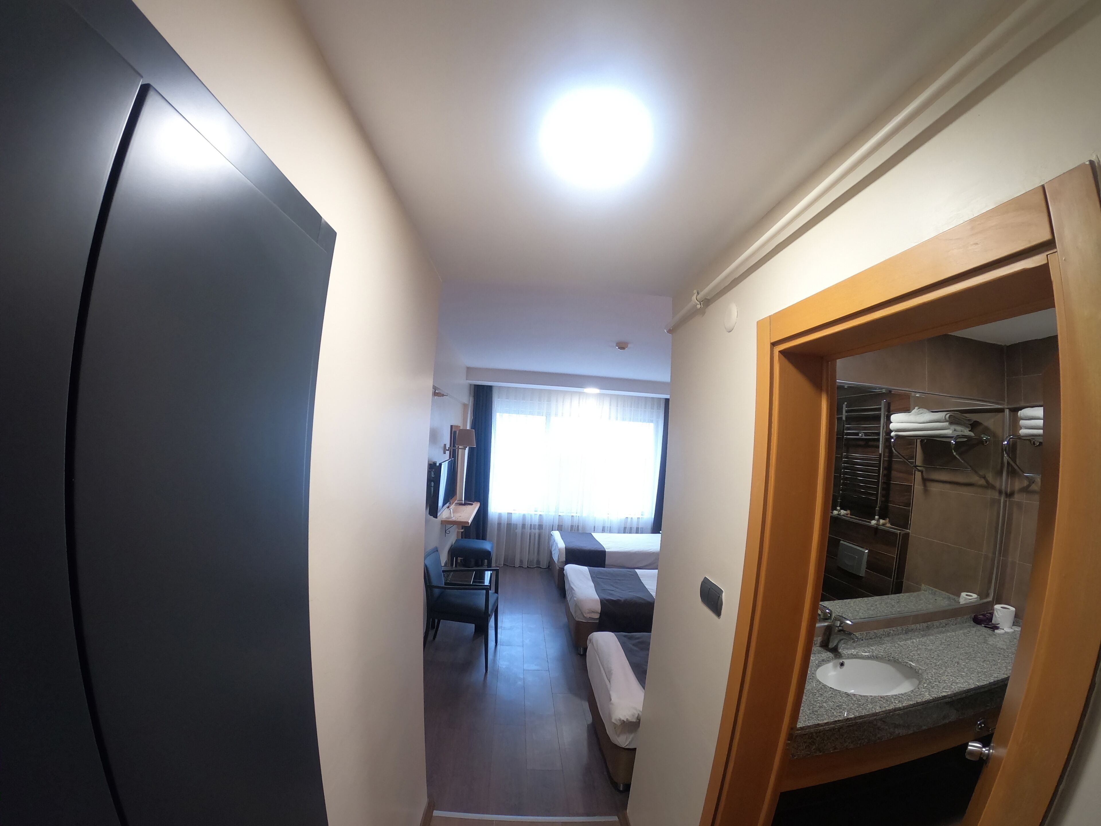 A compact hotel room with a kitchenette, a small seating area, and a bathroom with a mirror and sink.