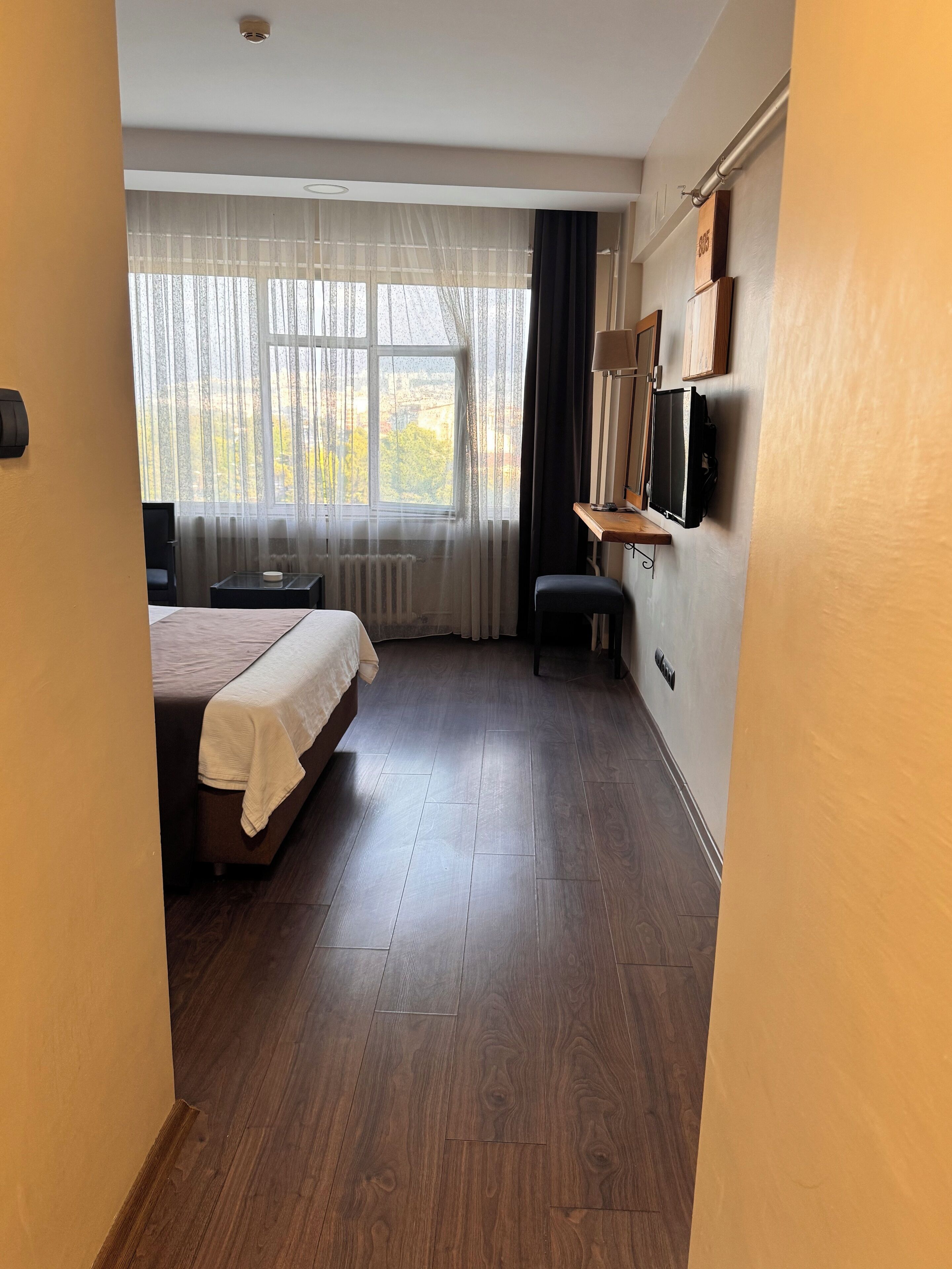 Habitación de hotel con cama, escritorio, silla, televisor y ventana con cortinas.