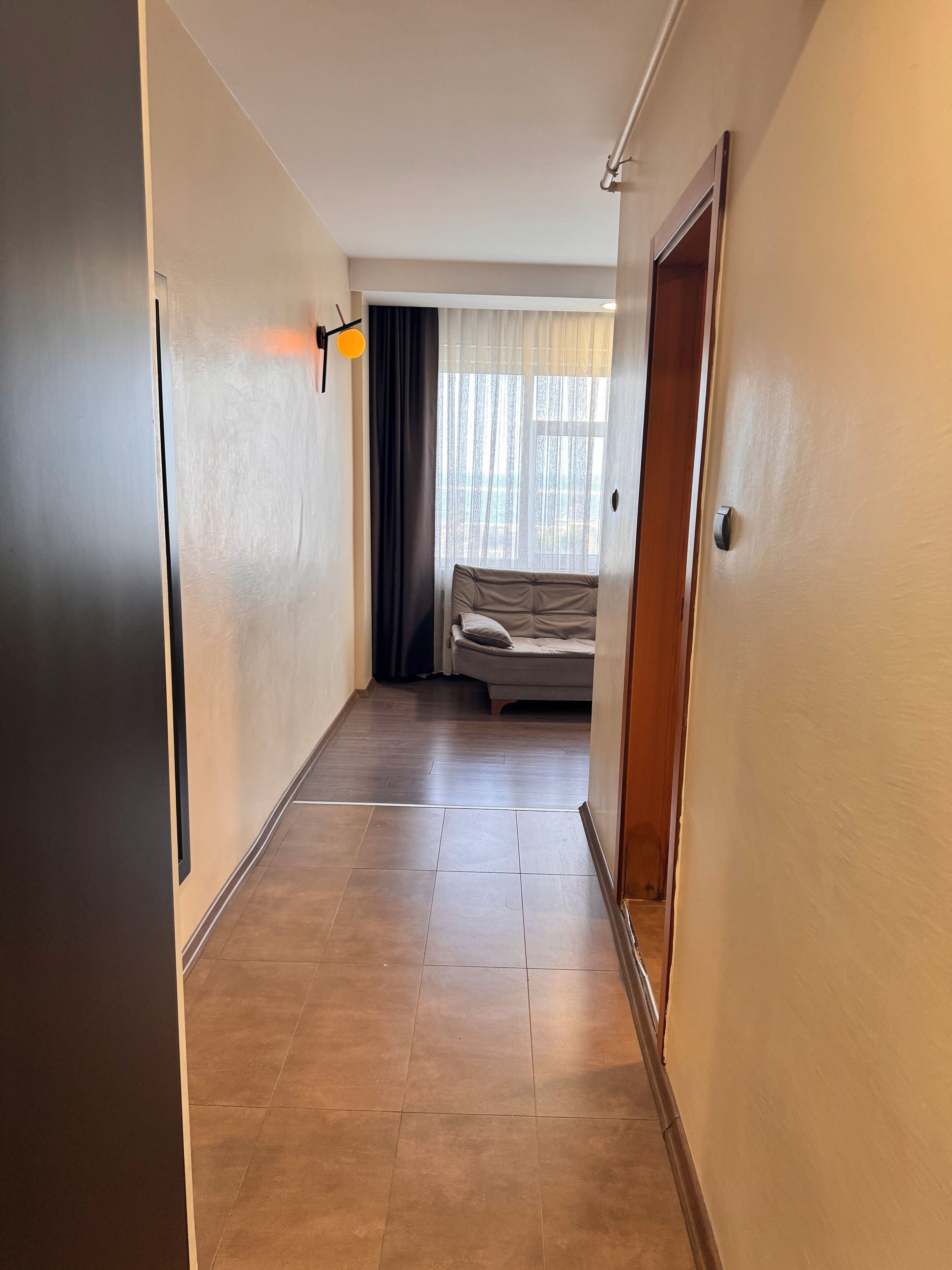 A hallway with a bed, a window with curtains, and a door.