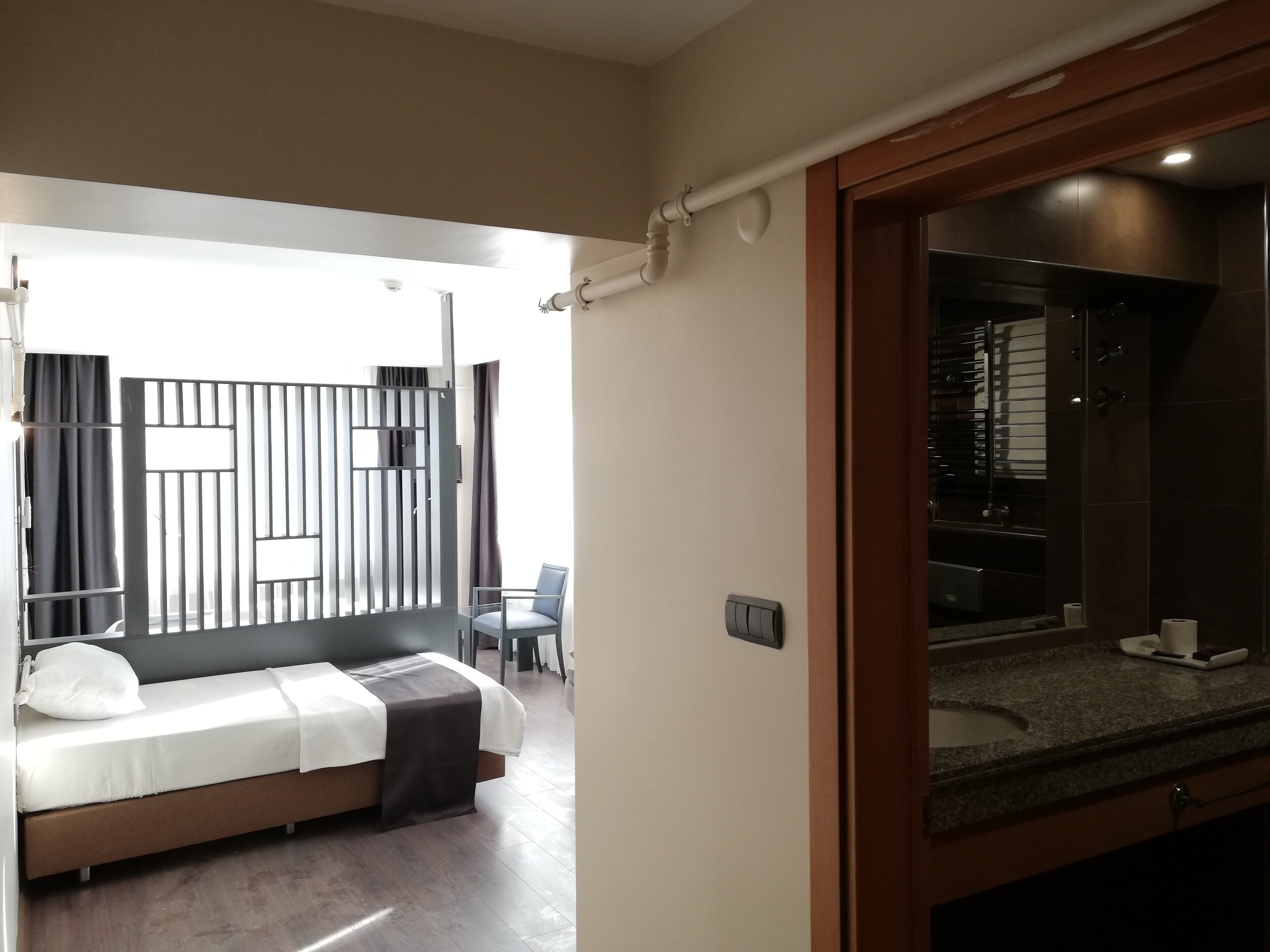 Ett modernt hotellrum med en säng, ett litet bord, en stol och ett badrum som syns genom en öppen dörr.