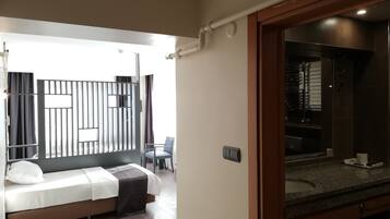 Ett modernt hotellrum med en säng, ett litet bord, en stol och ett badrum som syns genom en öppen dörr.