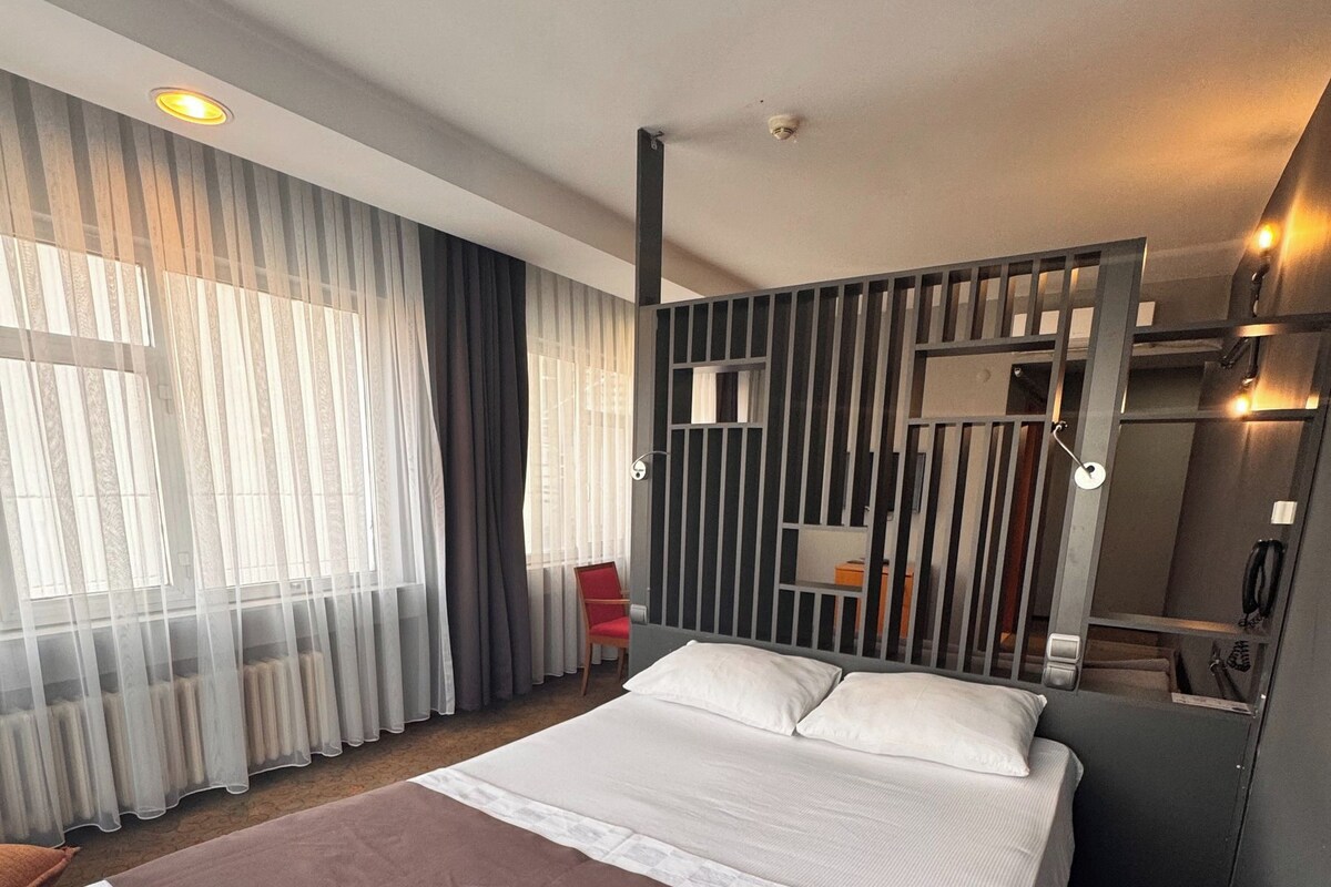 Una habitación de hotel con una cama grande, una silla roja, un espejo y una ventana con cortinas.