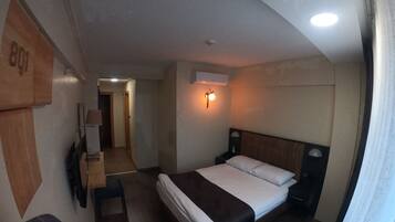 Una camera d'albergo con un letto, un comodino, una lampada e un condizionatore d'aria.