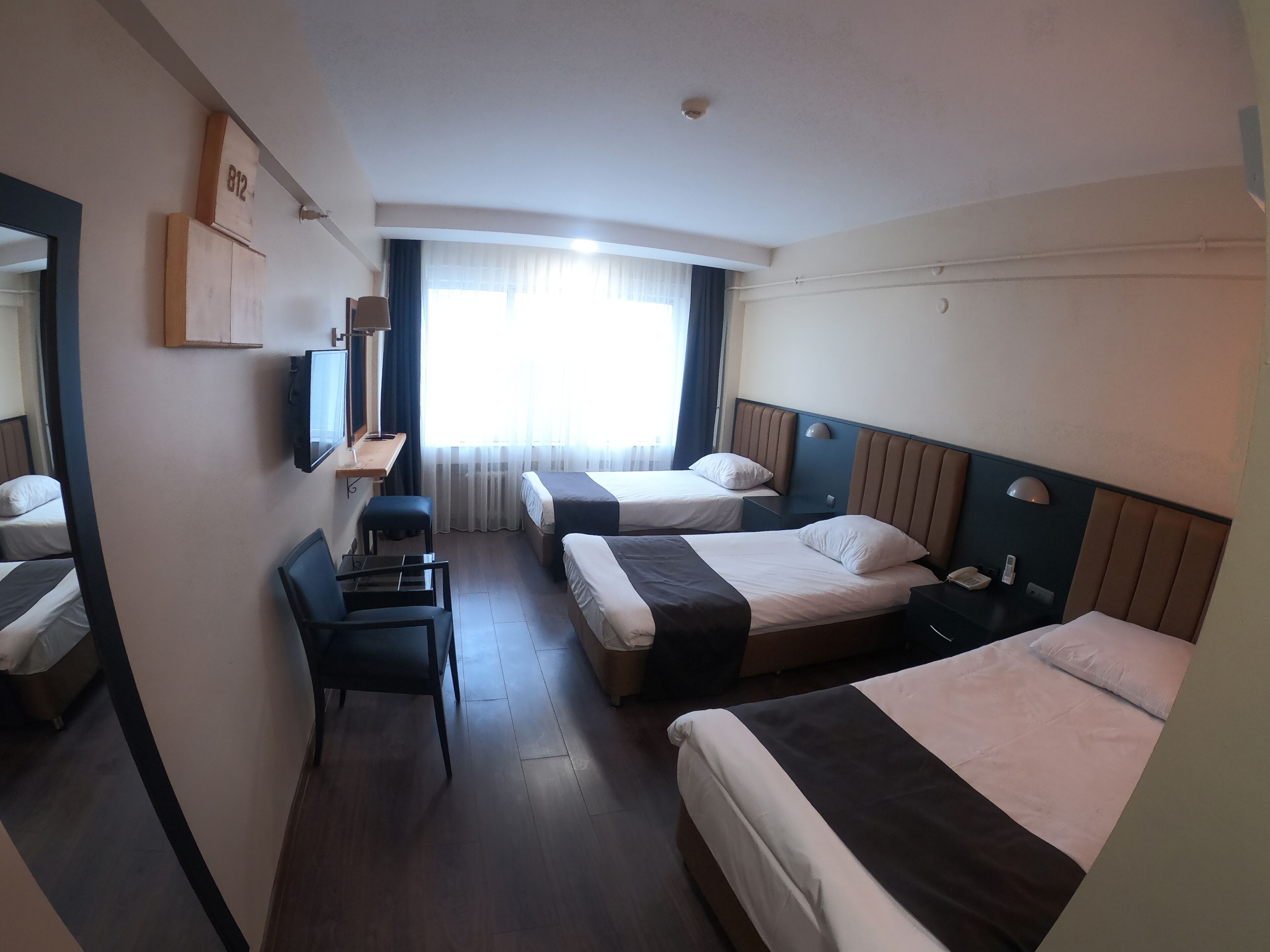 Une chambre d’hôtel avec deux lits, un bureau, une chaise et une grande fenêtre avec des rideaux.
