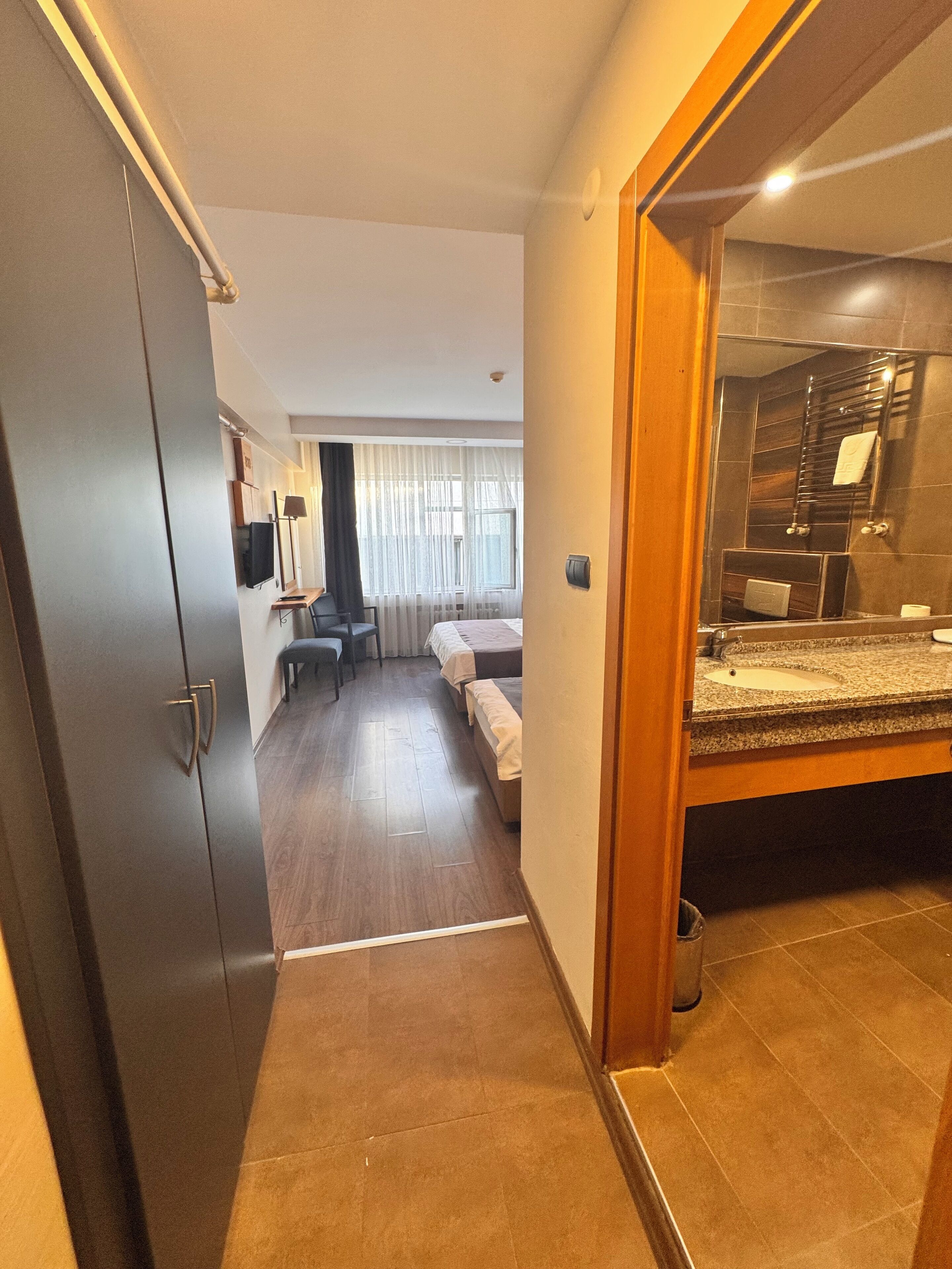 A hotel room with a bed, a desk, a chair, a TV, and a bathroom with a sink and mirror.