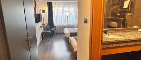 A hotel room with a bed, a desk, a chair, a TV, and a bathroom with a sink and mirror.