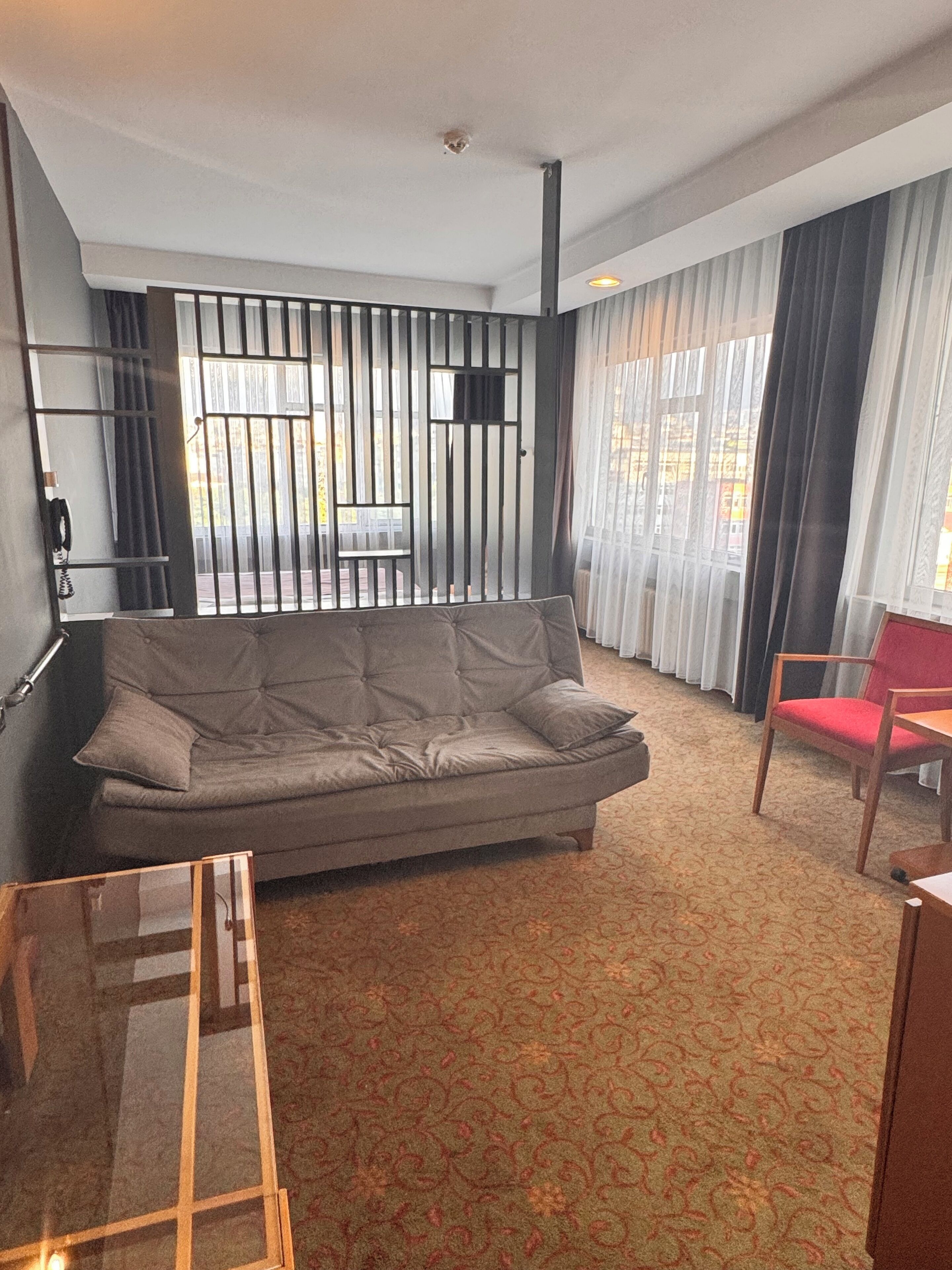Una habitación de hotel moderna con un sofá gris, una silla roja y una alfombra estampada.