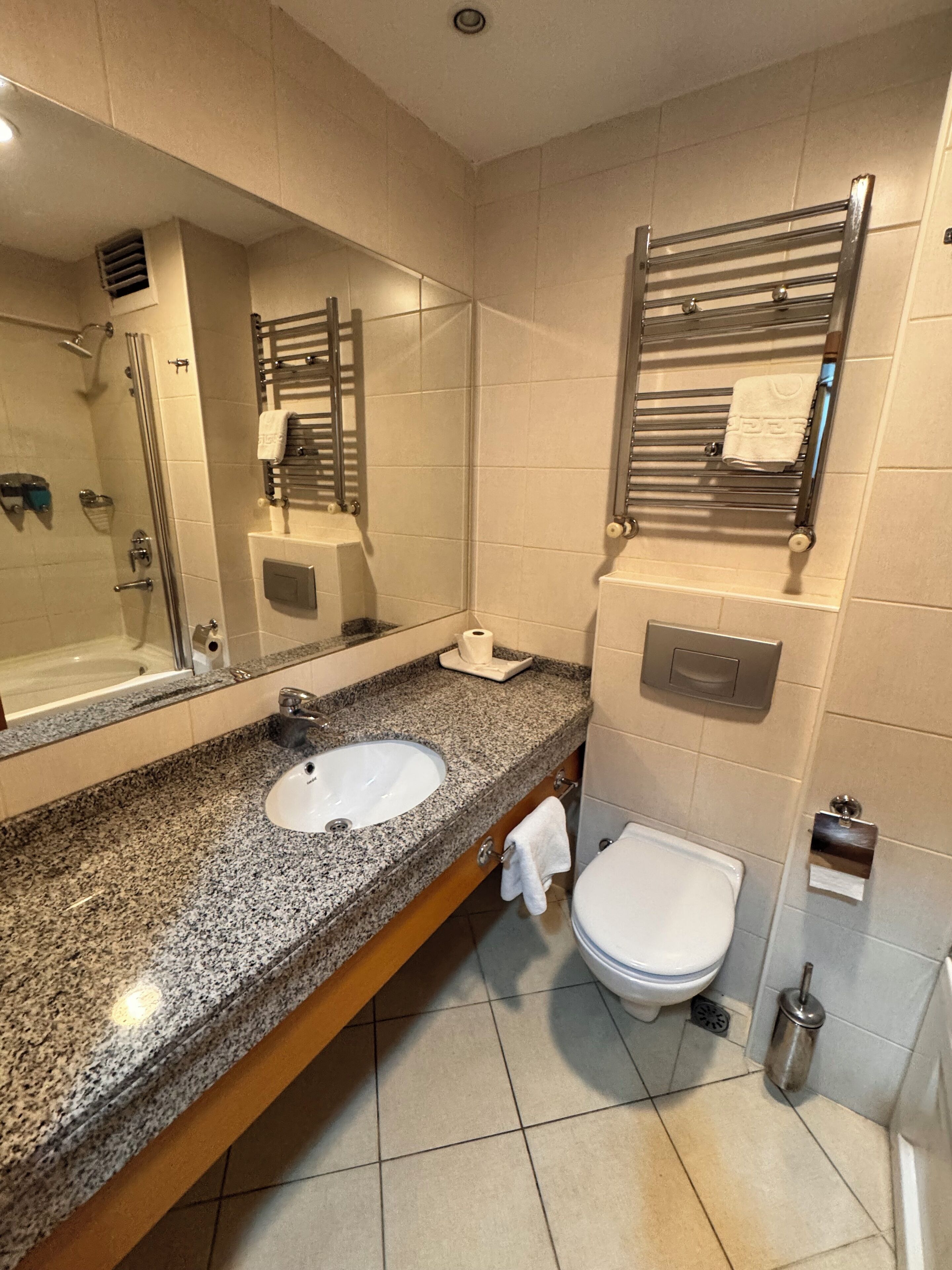 A modern bathroom with a granite countertop, a white sink, a toilet, and a large mirror.