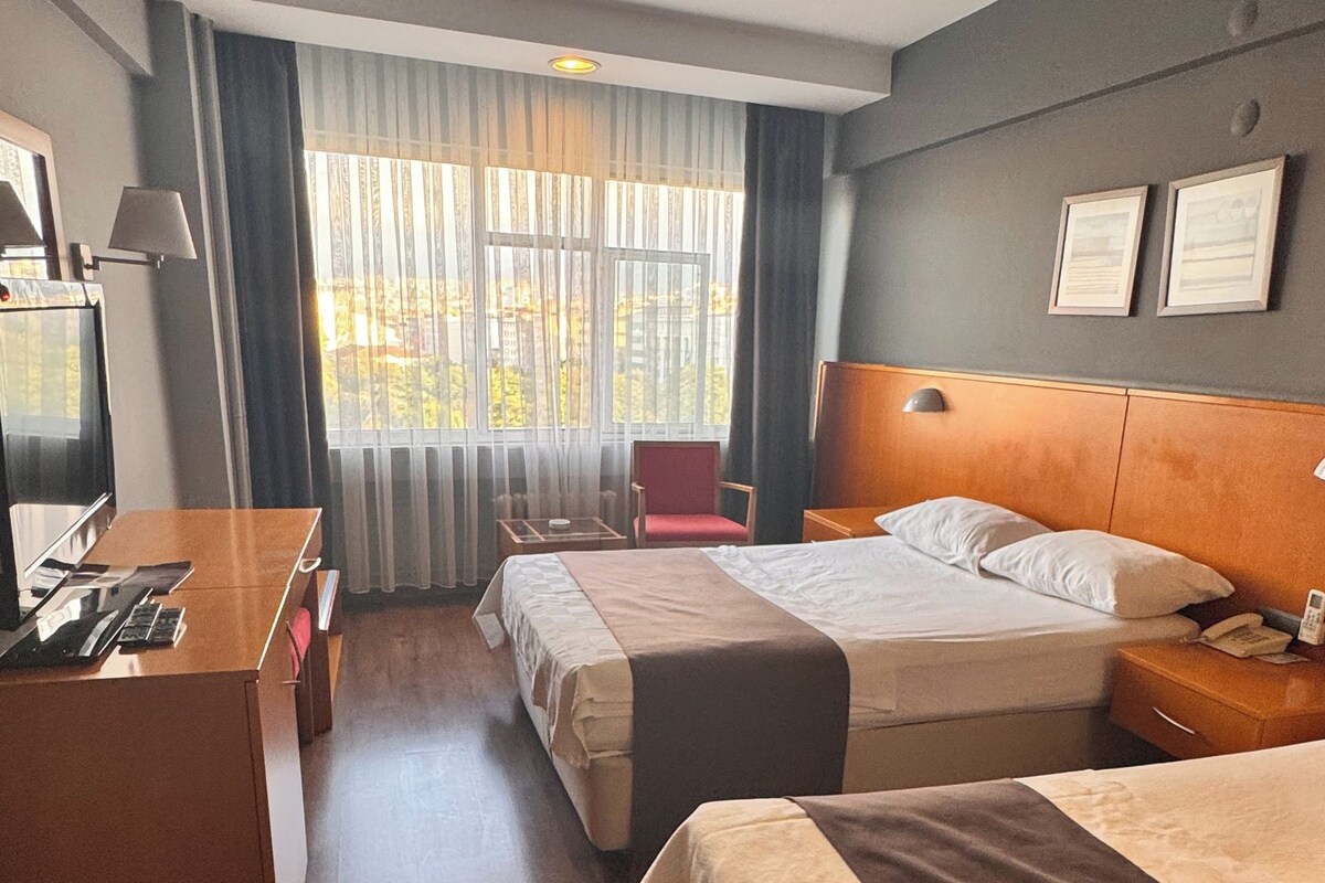 Habitación de hotel con dos camas, un escritorio, una silla, un televisor y una ventana con cortinas.