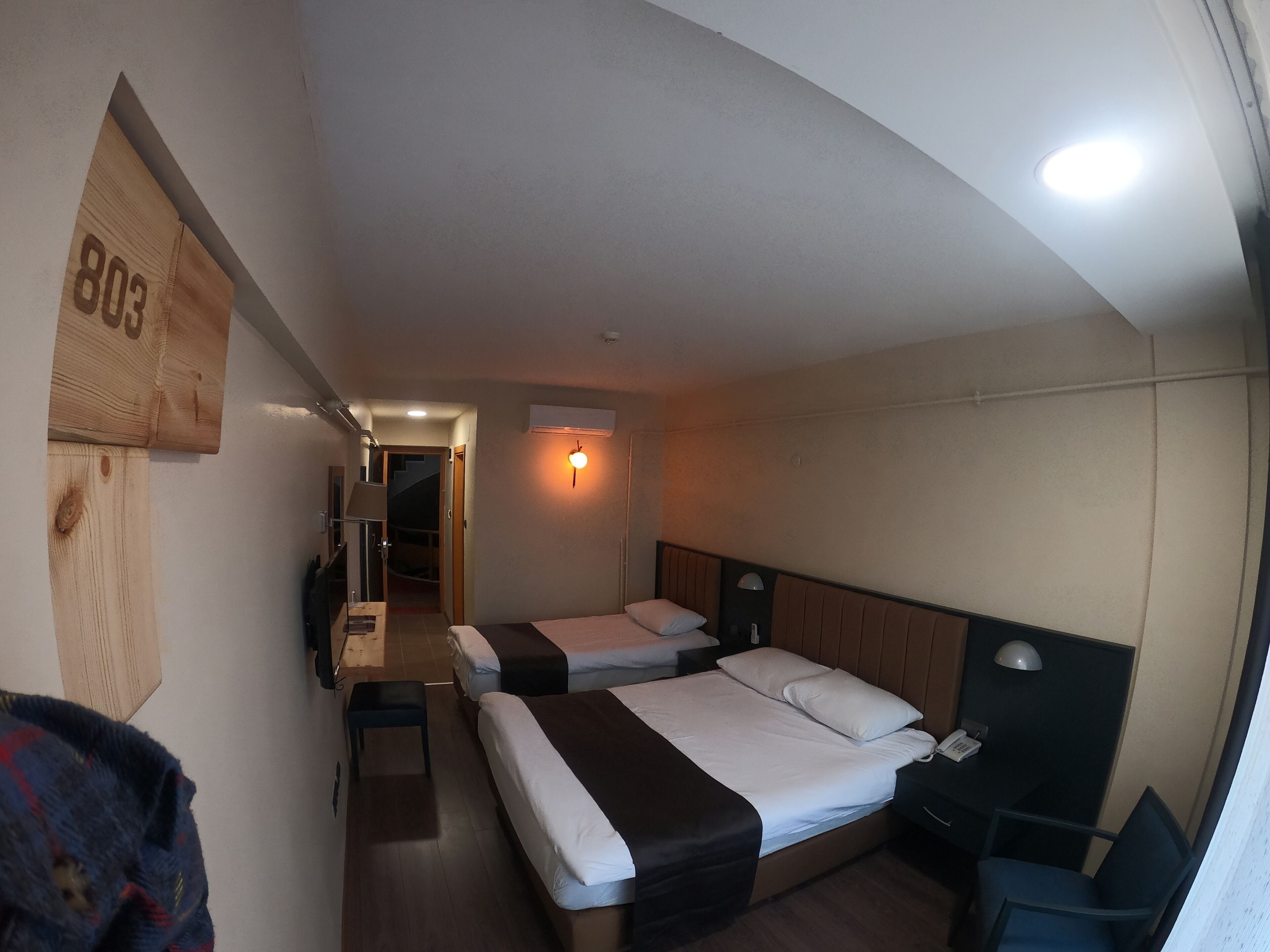 Quarto de hotel com duas camas, uma escrivaninha, uma cadeira e uma mesinha.