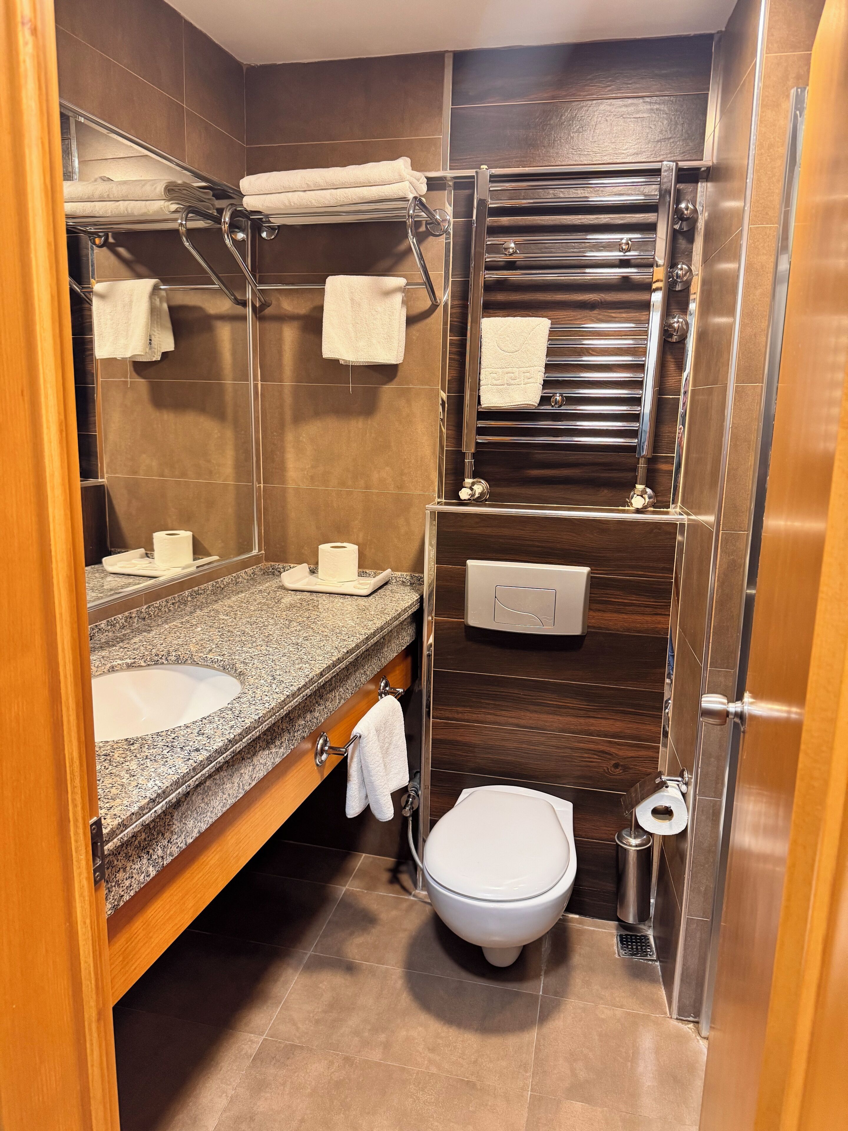 Un baño pequeño con encimera de granito, un lavamanos blanco, inodoro y toallero.