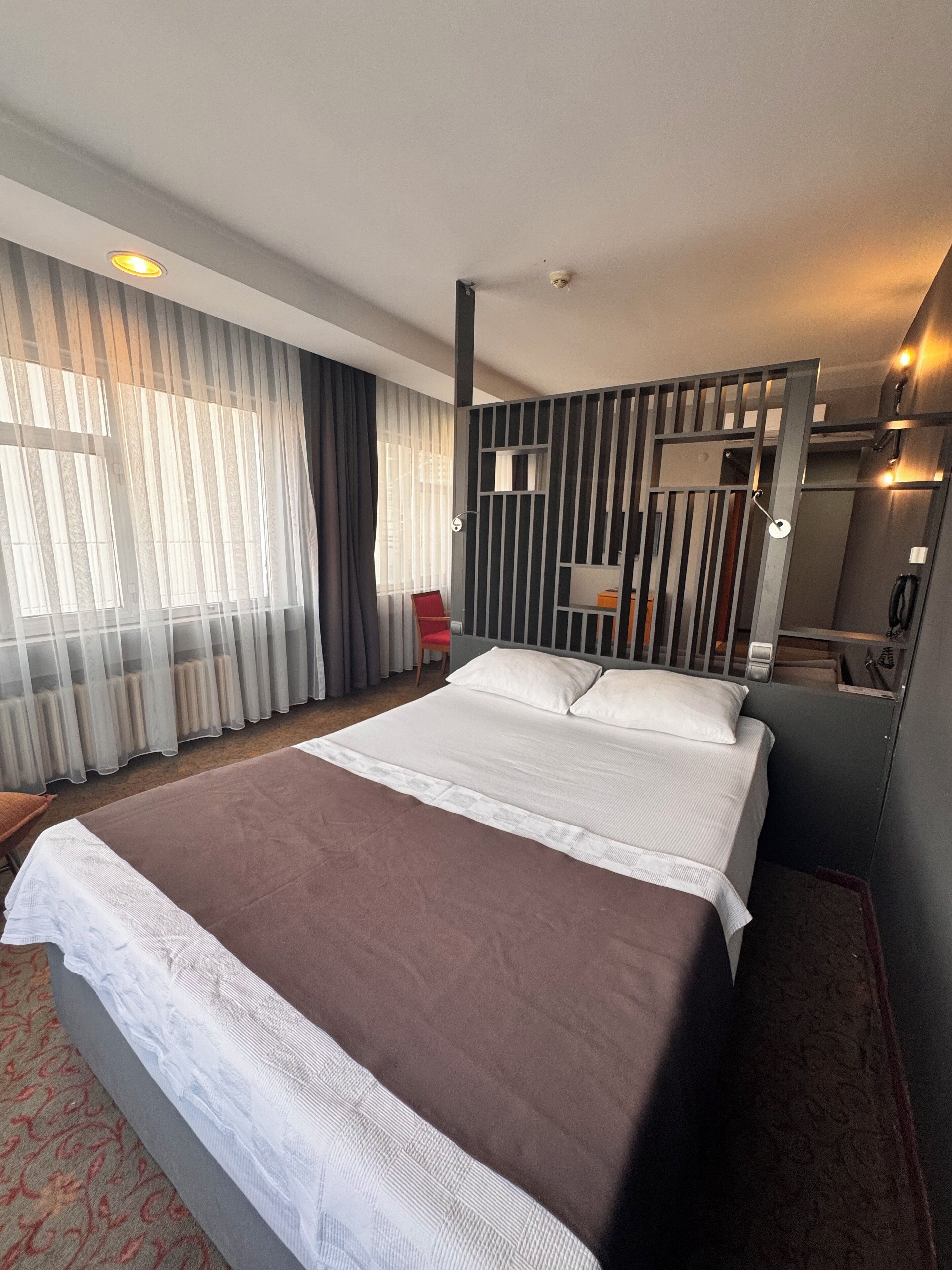 A modern hotel room with a large bed, a red chair, a desk, and a mirror.