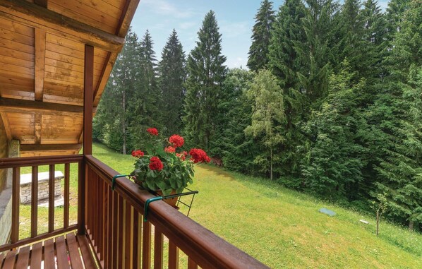Een houten balkon met uitzicht op een bebost gebied en een tuin met rode bloemen.