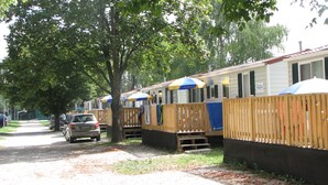 A row of mobile homes with wooden fences, a gravel path, and a parked car.