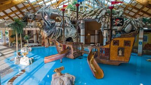 A nautical-themed indoor play area with slides, climbing structures, and a shipwreck backdrop.