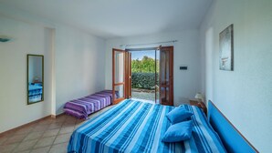 A bedroom with a large bed, a smaller bed, a mirror, and a view of the garden through an open door.