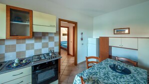 A compact kitchen with a gas stove, oven, and wooden cabinets. A dining table with chairs is in the adjacent room.