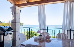 A patio with a grill, white chairs, a table with a flower vase, and a view of the sea. - Stunning home in Loviste (Loviste)