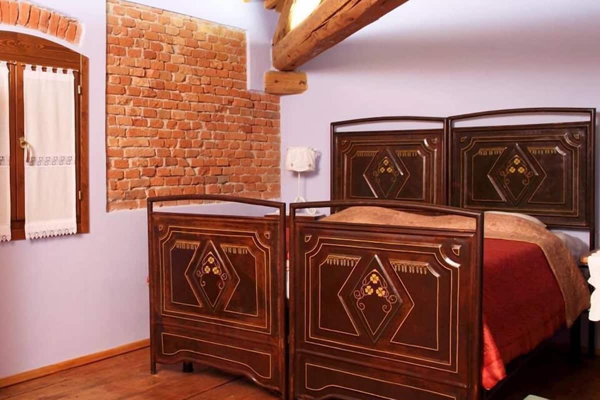 A bedroom with a wooden bed frame, a brick wall, and a wooden ceiling.