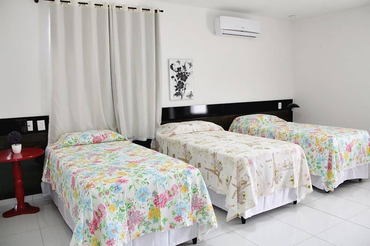 A hotel room with two single beds, a red side table, and a white air conditioning unit on the wall.