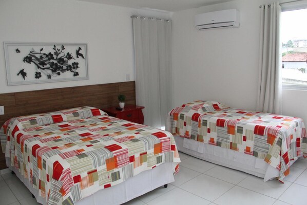 A hotel room with two beds, a wall-mounted air conditioner, a window with curtains, and a wall art piece. - France Hotel (Guarabira)