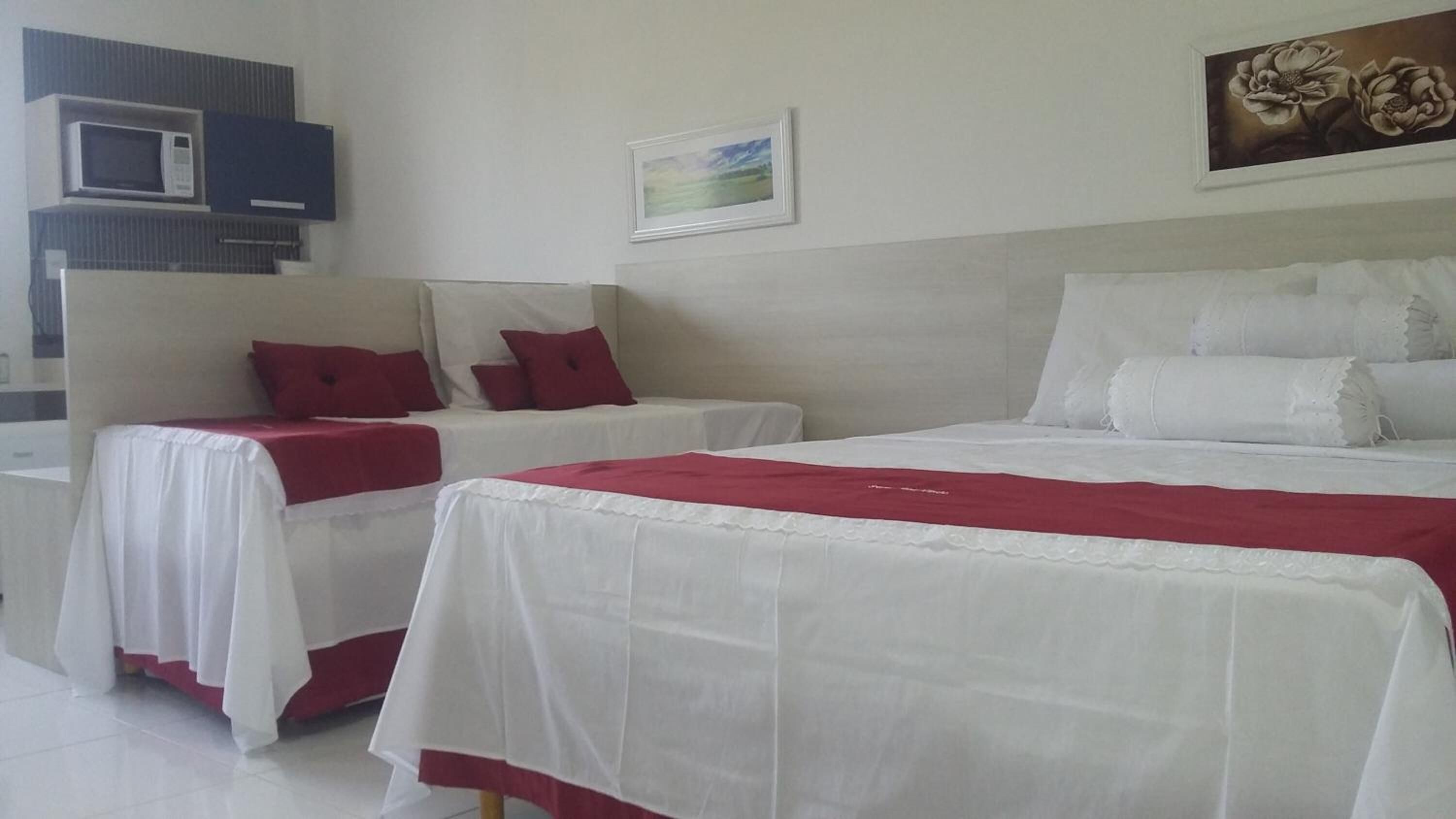 Habitación de hotel con dos camas, cada una con ropa de cama blanca y detalles rojos. Hay un microondas y un cuadro en la pared.