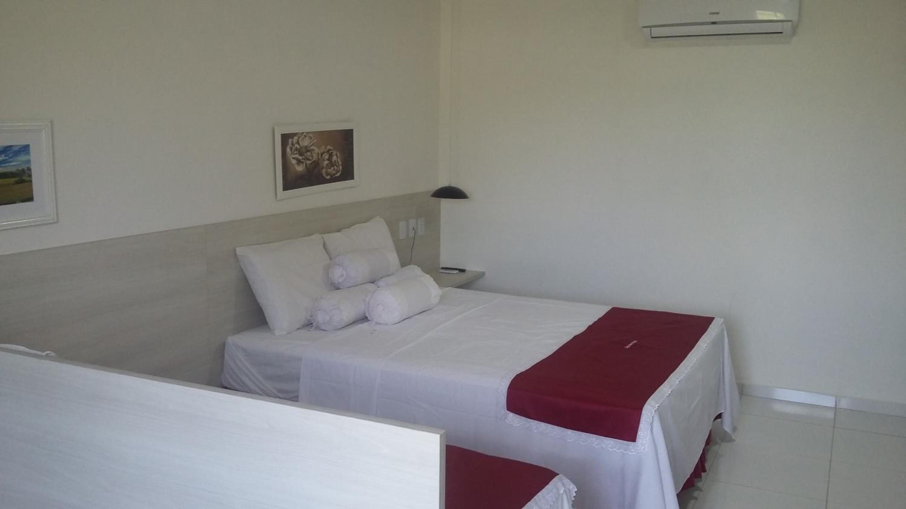 A hotel room with a bed, a nightstand, a lamp, and a wall-mounted air conditioner.