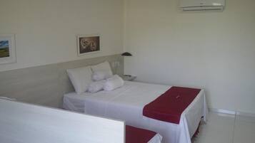 A hotel room with a bed, a nightstand, a lamp, and a wall-mounted air conditioner.