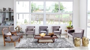A modern living room with large windows, grey armchairs, a wooden coffee table, and a grey shag rug. - France Hotel (Guarabira)