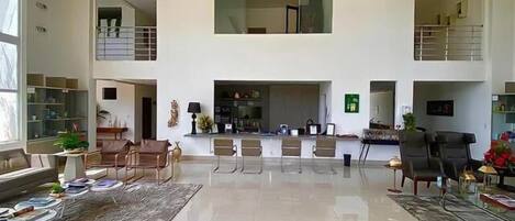 A spacious living area with a high ceiling, a fireplace, and a seating arrangement.